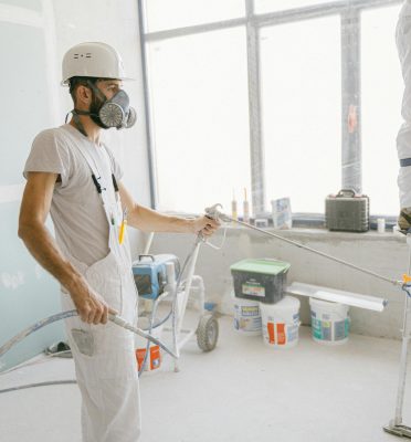 Two construction workers wearing protective gear and painting interior walls for a renovation project.