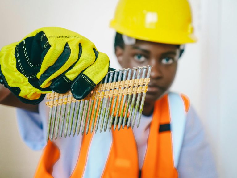 Close-up of a construction worker holding a row of steel nails while wearing protective gear.
